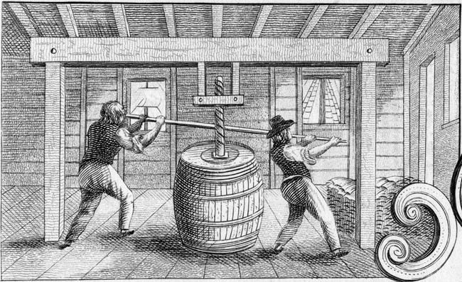 Screw pressed used to pack cod Black and white image of two people packing cod into a barrel.