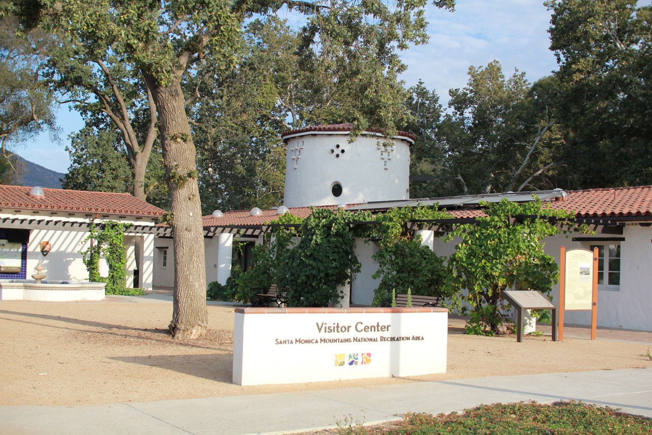 A white building with a terra cotta roof and a sign in front saying "Visitor Center"