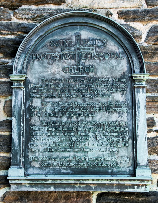 Metal plaque, with curved top, with inscription, affixed to a stone wall