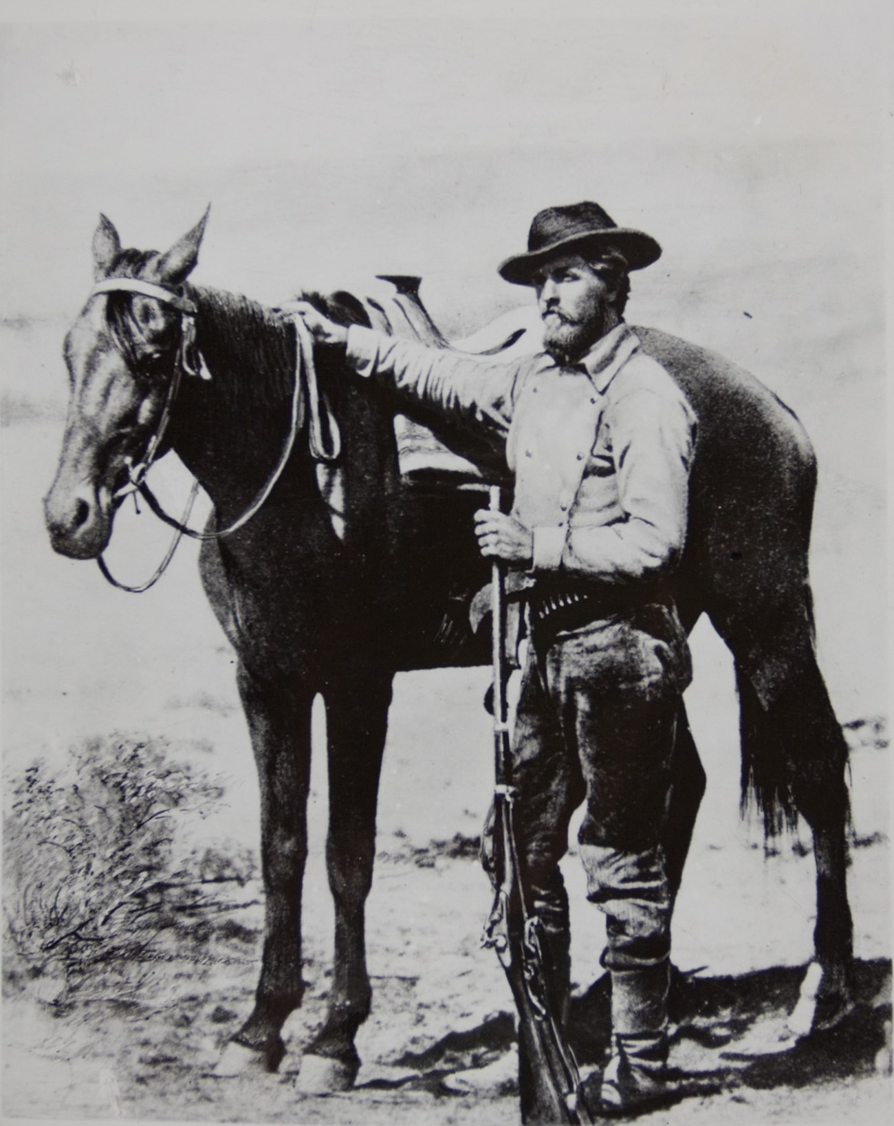 A bearded man stands holding the reins of a horse.