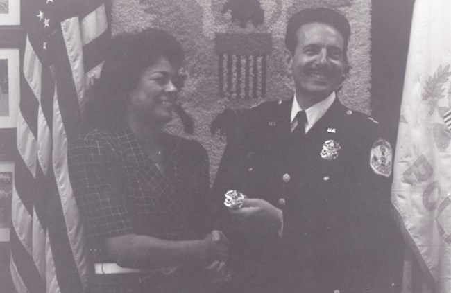 Raquel Manso shakes hands with a man in uniform as he hands her a police badge.