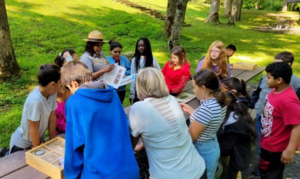 A woman in a park ranger uniform interacts with students at a table outside.