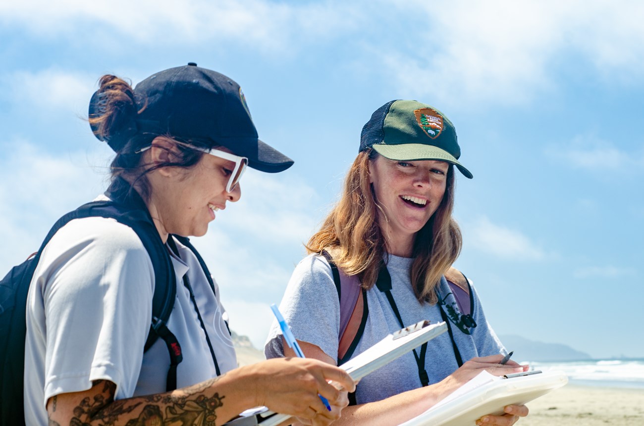 Rachel with Wildlife Intern Anna Arce on a snowy plover survey Rachel on Ocean Beach, smiling as she converses with a wildlife intern. Both carry clipboards for recording western snowy plover data.