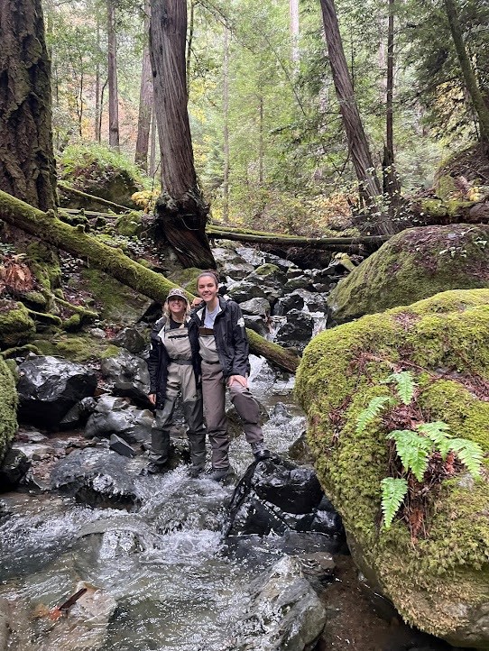 Tara and Natale Two young people standing in the middle of a brisk, rocky creek, surrounded by towering coast redwoods.