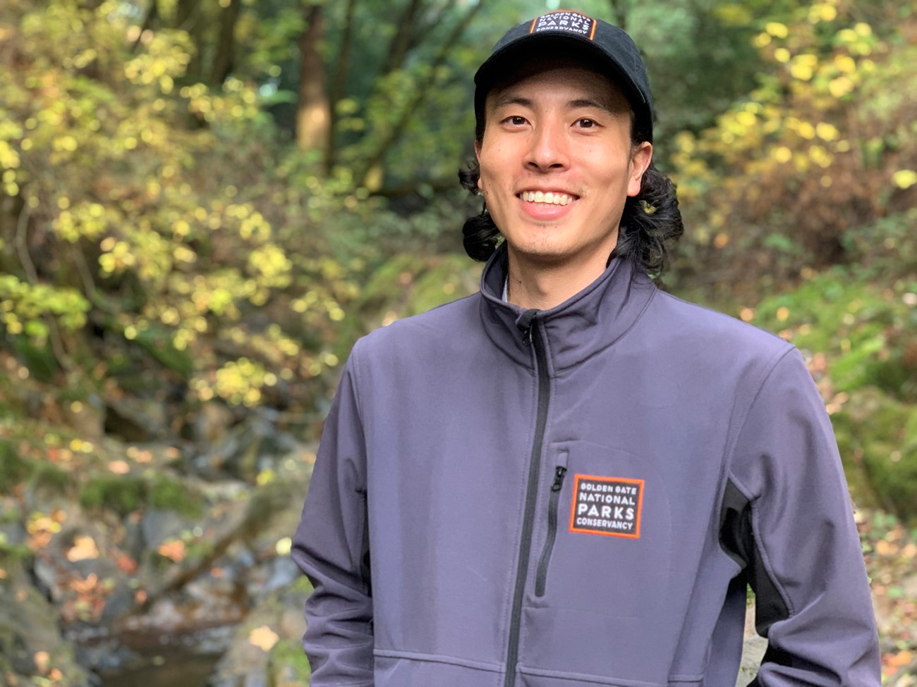 Alex Iwaki Portrait of Alex in the forest, smiling at the camera.