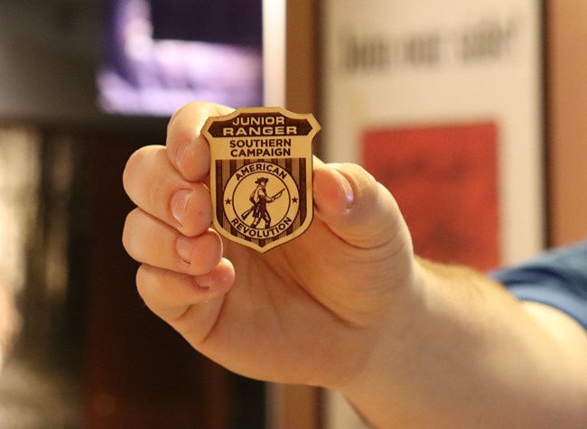 Hand holds Southern Campaign of the American Revolution Junior Ranger Badge