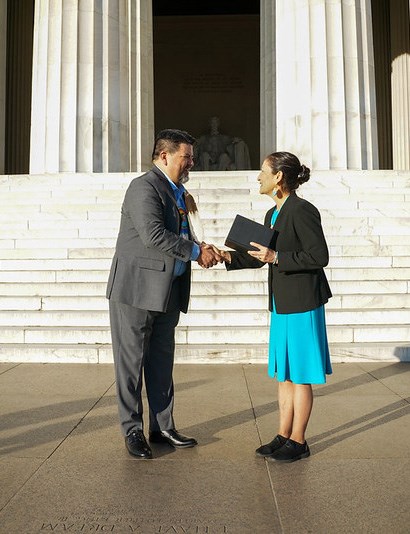 a man and woman shake hands in front of the Lincoln Memorial