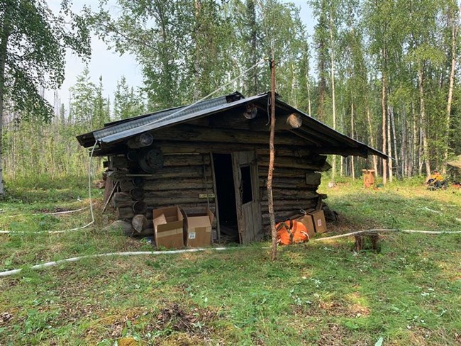 Sam Creek Cabin with sprinkler protection. A small log cabin in the woods surrounded by fire equipment and hoses.