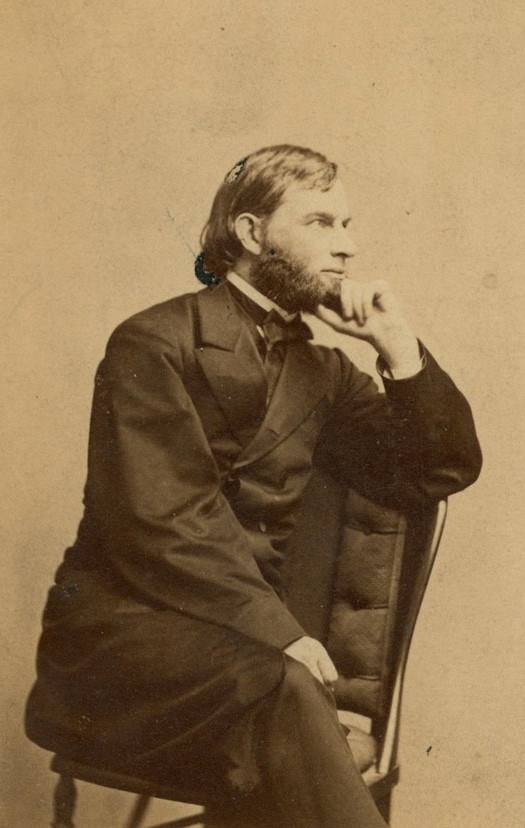 Studio portrait of man seated in chair, looking to his left, resting chin on hand