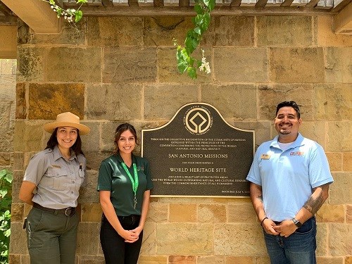 two women and a man, intern, posing in front of san antonio missions' sign