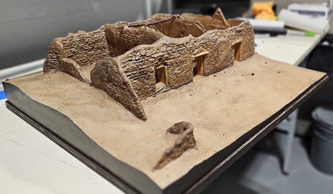 San Cayetano de Calabazas model A 3D printed plastic model sits on a desk. The model is roofless showing the many colors of the adobe brickwork.