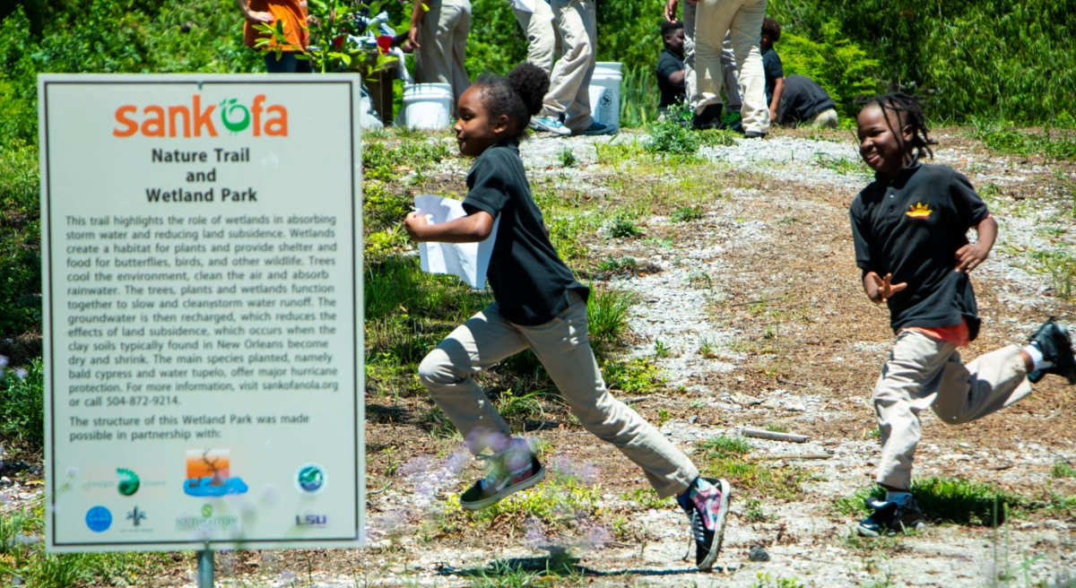 Children running past a sign that reads Sankofa Nature Trail and Wetland Park Children running past a sign that reads Sankofa Nature Trail and Wetland Park