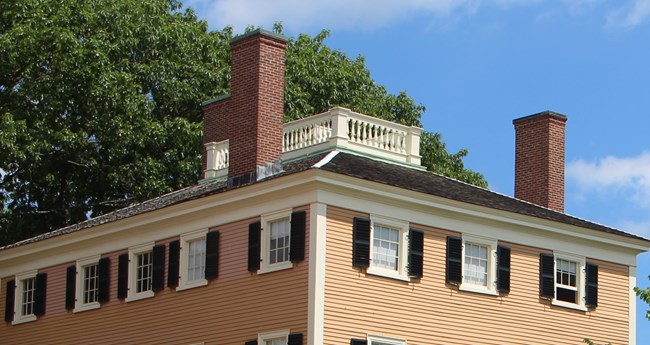 A white fenced enclosure on the roof of a yellow house.