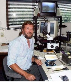 Santucci_figure_4_Ted_Fremd_REV Photograph of a man sitting in front of monitors and scientific equipment such as microscope.