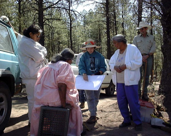 Sarah Herr working with Apache knowledge keepers, US Forest Service and an ethnographer. Collection of collaborators and knowledge keepers looking at a map of an archaeological site