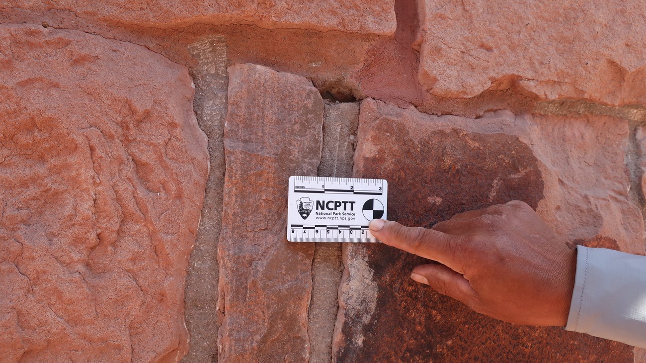 Uniformed man's hand holding a scale card against a building with old, orange-brown bricks.