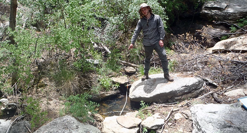 Scarlet Spring A person pointing at a small pool of water surrounded by large rocks in a drainage.