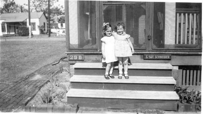 two young girls in dresses stand on porch steps
