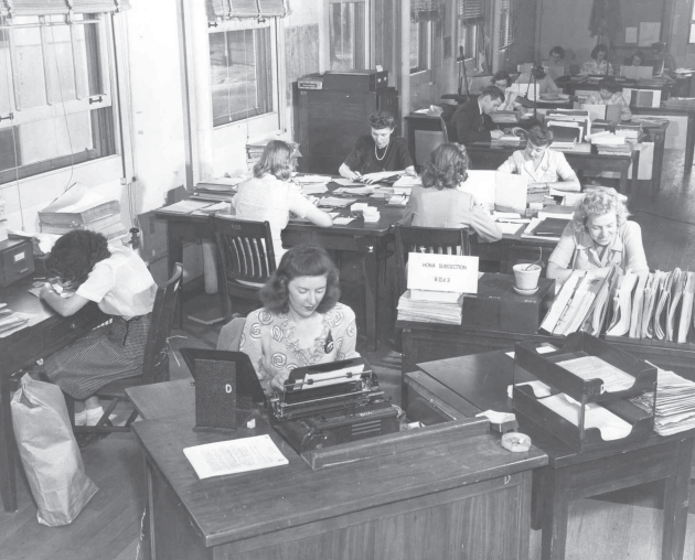Black and white image of girls working on desks. Ann is pictured at the far-right desk, in Arlington Hall