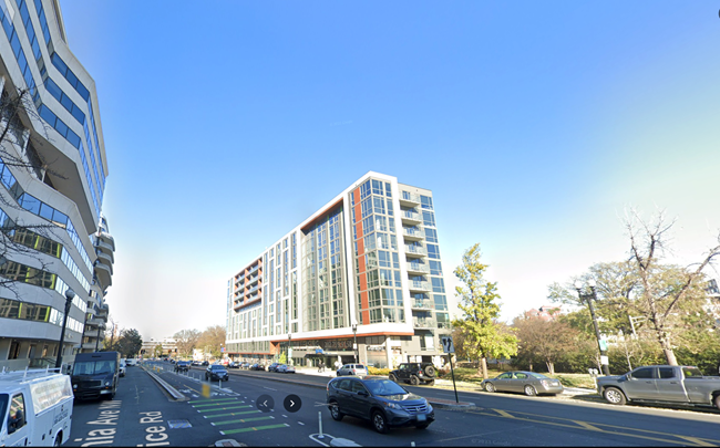 A view from the street (with cars parked, and driving along) of a tall, glass-windowed building.