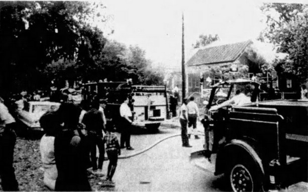 A group of people watching fire fighters put out a house fire.