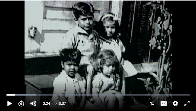 Screenshot of a video frozen on an image of four young children, two boys and two girls.