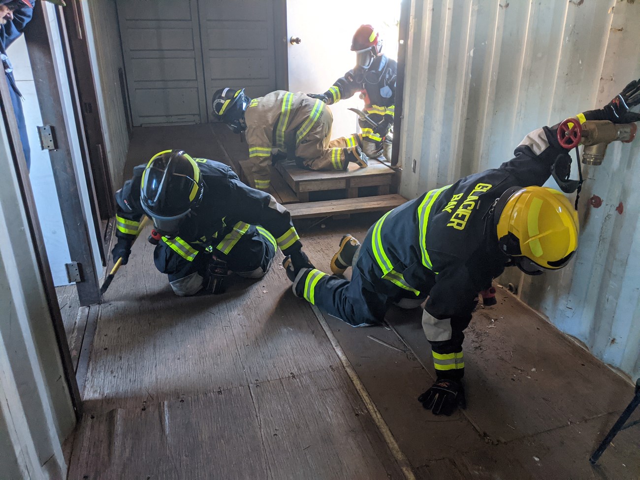 Structural firefighters search building for victim. Four firefighters crawl into a trailer feeling doors.