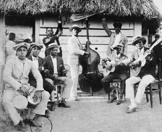 Eight Afro-Latino men pose for a photo holding various instruments, from drums, double base, and guitars.