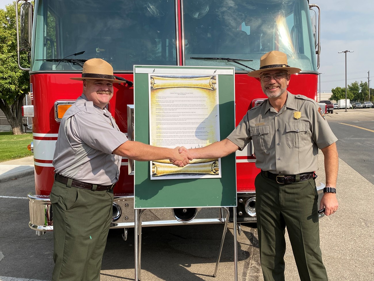 Shane Crutcher and Chad Fisher sign proclamation Two people shake hands in front of a fire engine with a board holding a sign.
