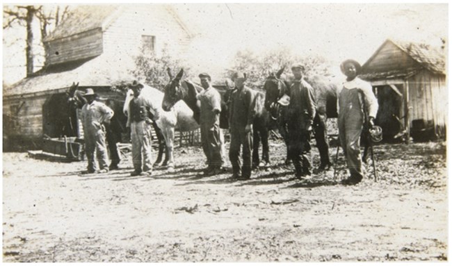 Men in working clothes standing in a line. One man is on crutches.