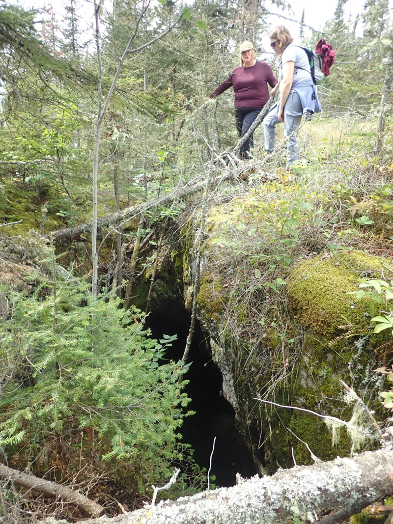Two people stand over an Indigenous copper-mining pit on Isle Royale