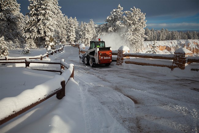 Skid Steer Sunset Point A skid-steer tractor snow blows snow along a sidewalk