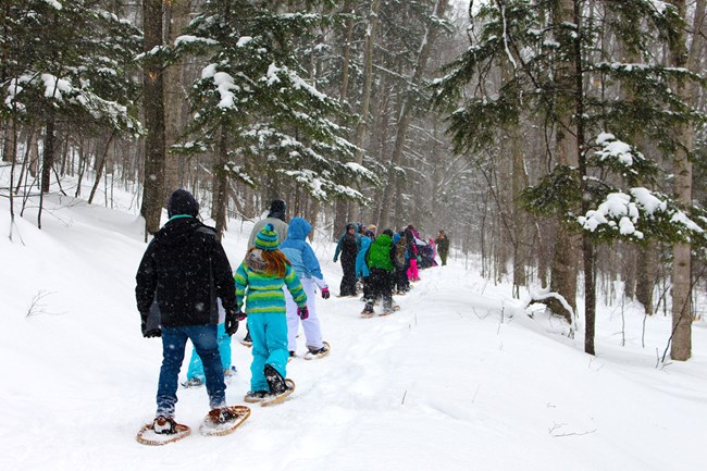 Sleeping Bear Dunes Heritage Trail A group of children and adults in winter coats use snowshoes to walk a snowy forest trail.