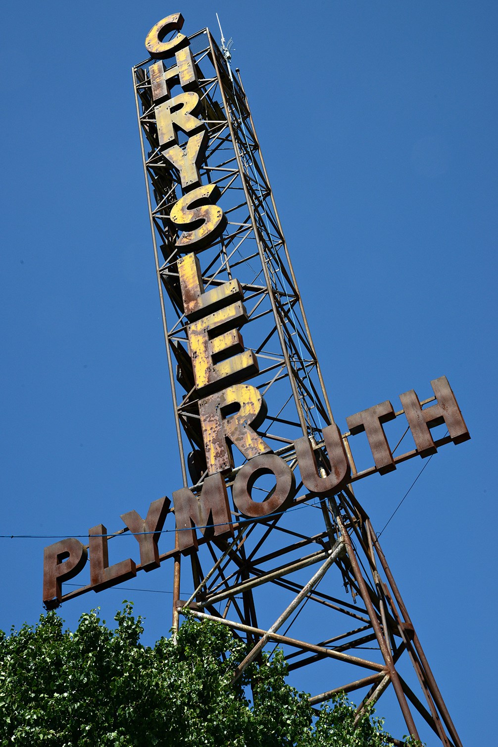 Beard Motor Company Tall narrow tower made of rods with vertical text reading Chrysler and Plymouth horizontally.