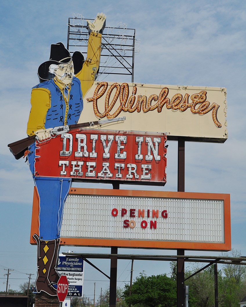 Winchester Drive In Larger than life cowboy waving holding a rifle text reads Winchester Drive In Theatre and marquee reading Open Soon.