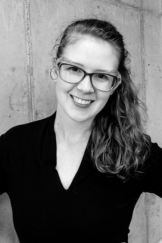 Smiling woman wearing glasses wearing a dark blouse with long wavy hair pulled back and over one shoulder. Smiling woman wearing glasses wearing a dark blouse with long wavy hair pulled back and over one shoulder.