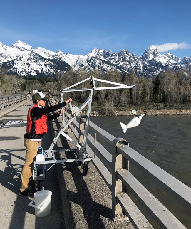 A person operating a small Crane on a bridge with a sampler hooked to it