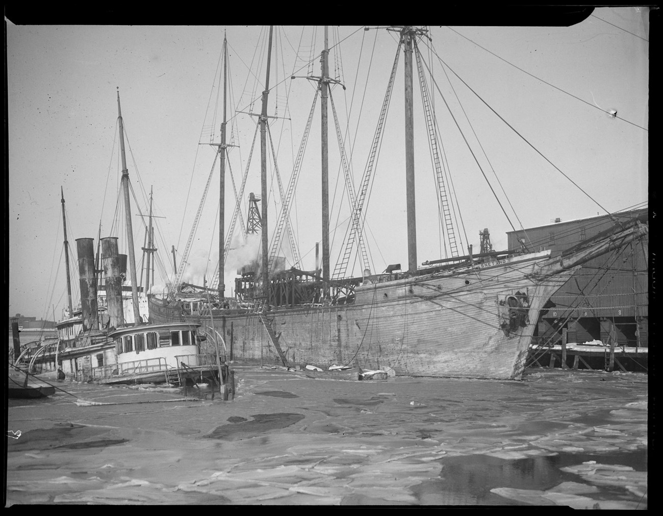 Snetind-Leslie Jones Collection-BPL four-masted schooner along a dock with a tugboat next to it