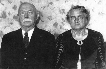 Picture of a bald man with white moustache and woman with glasses.