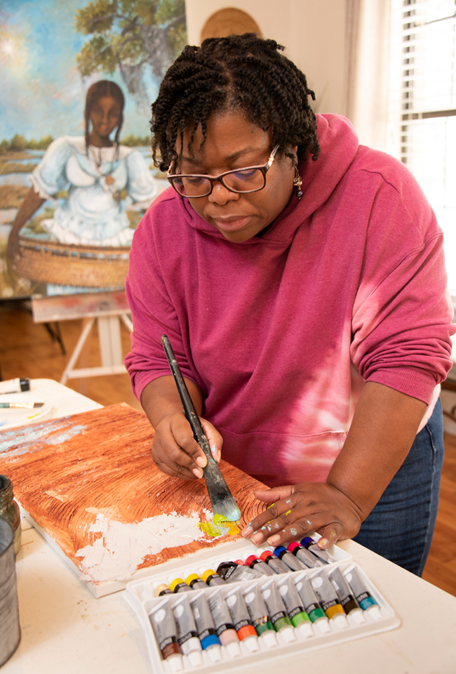 Sonja Griffin Evans Sonja stands at a table painting on a canvas.