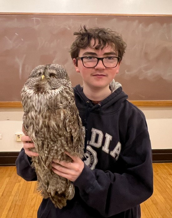 A young man wearing glasses holds a taxidermy owl