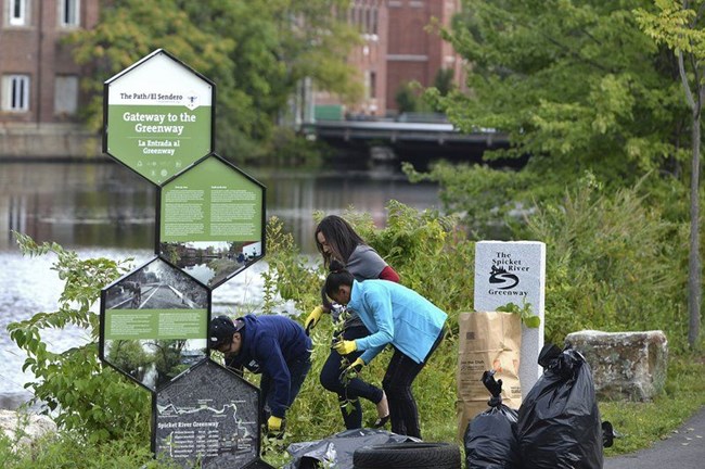 Volunteers help with gardening at the Gateway to the Greenway interpretive sign.