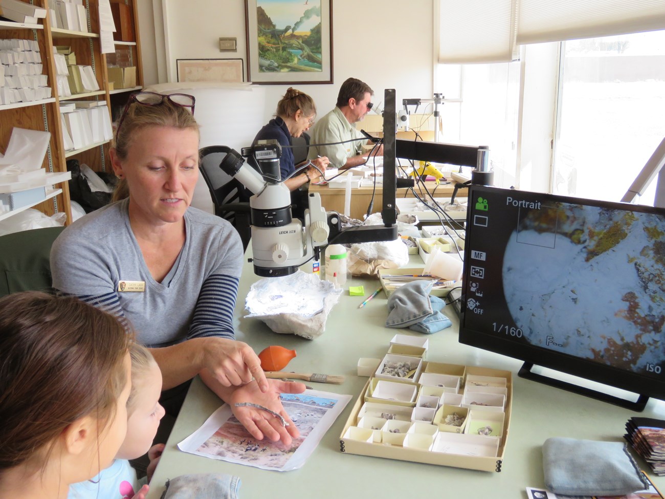 photo inside a fossil lab with paleontologist showing children some fossil specimens