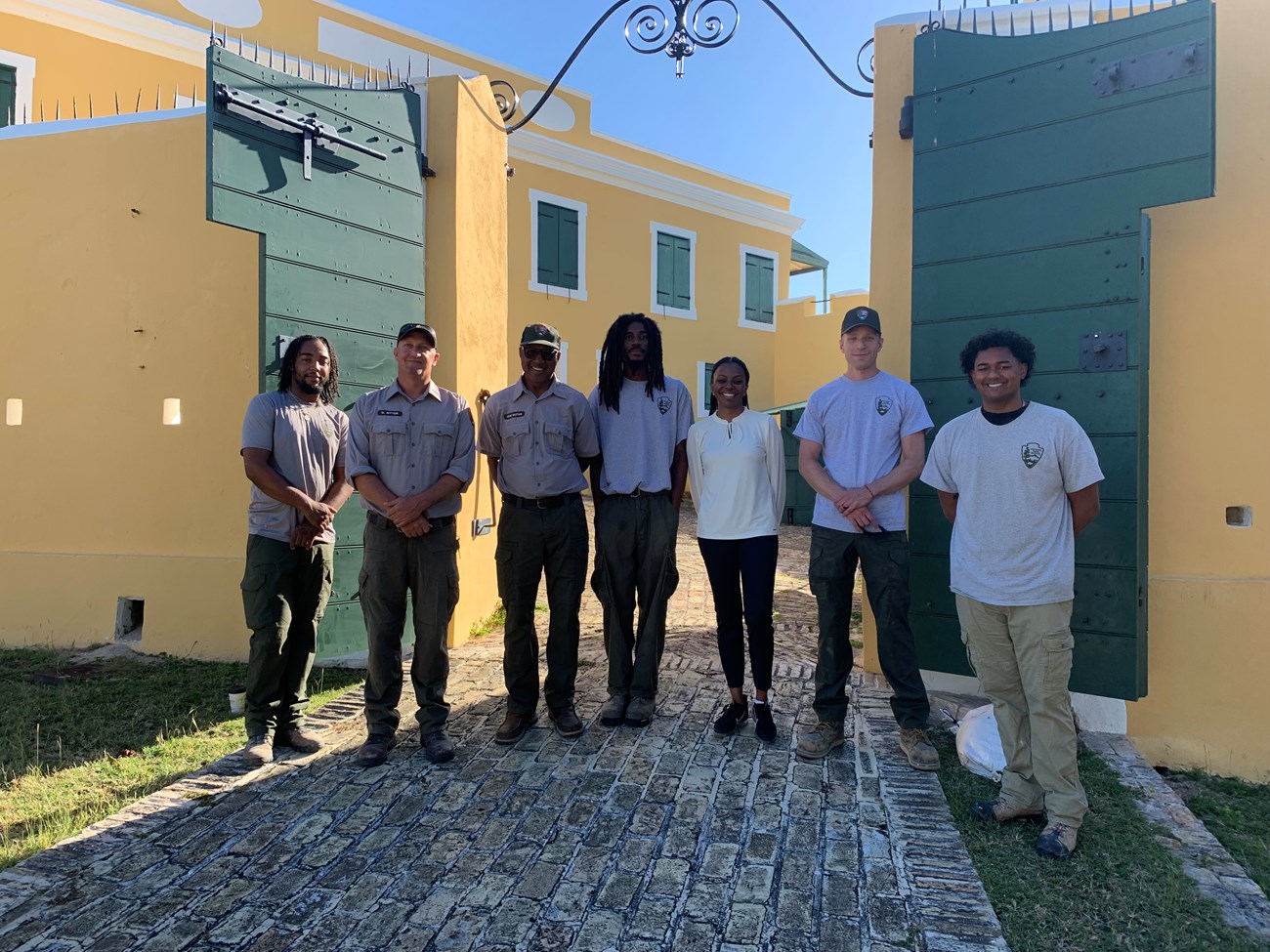 St Croix and San Juan Caribbean Crew Assembles for the first time. Seven NPS staff stand shoulder to shoulder in a line in front of a building at Christianstead National Historical Park.
