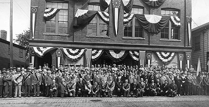 A large group of people gathered in front of three-story brick building on Derby Street