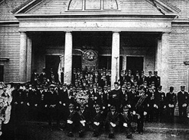 Black and white photo of members of the St. Joseph Society on the steps of a wooden church.