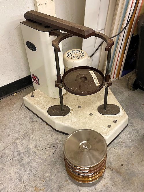 Stacked sieve shaker Big device with a round metal sieve tray-holder attached to two vertical metal bars connected at the top by a metal arm that can move both bars--and the tray--back and forth.