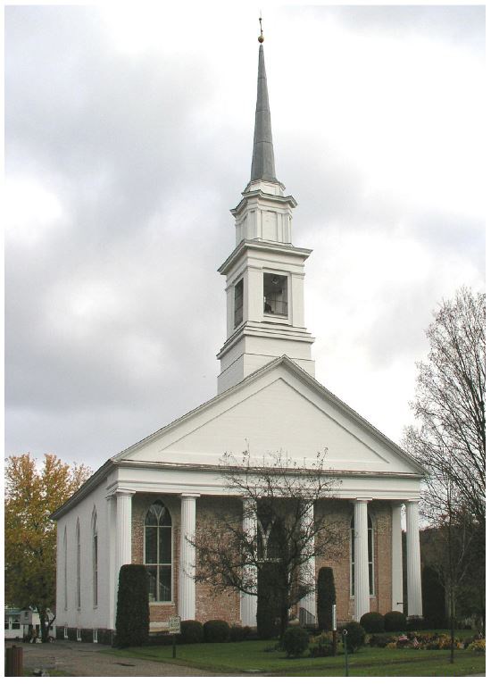 A 132-foot-tall  steeple sits atop a single-story white Greek revival church with six pillars with a pale brick entrance façade.
