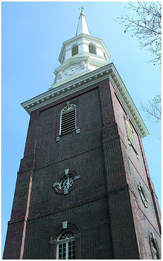 Closeup looking up the rectangular brick  tower supporting a tall white steeple.