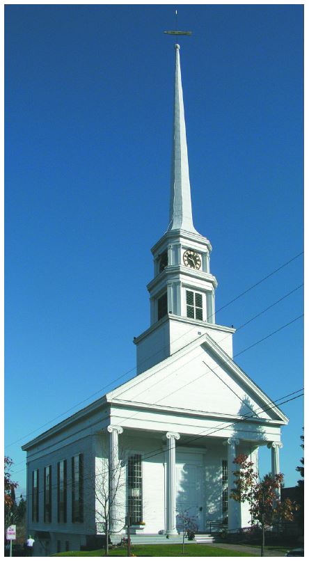 A white 90-foot-tall spire sits atop a steeple with a clock and belfry on a white Greek revival church with four columns in front.